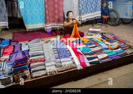 Une femme locale vend des tissus dans le marché nocturne de la rue piétonne dans le centre de Luang Prabang, dans le nord du Laos, dans le sud-est de l'Asie Banque D'Images