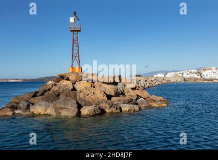 Feu à éclats vieux rouillé sur le mur de construction rocailleux à l'extrémité du port du village de Naoussa à l'île de Paros Cyclades Grèce.Mouche mouette au-dessus de la mer Egée calme, bl Banque D'Images