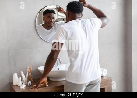 Un homme africain se brossant les cheveux en se tenant à l'appareil photo dans la salle de bains Banque D'Images