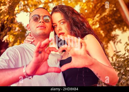 Un jeune couple aimant avec les mains forme un coeur immergé dans la nature au coucher du soleil Banque D'Images