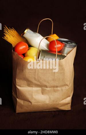 Produits dans un sac en papier sur fond de lin brun.Nourriture dans un service de livraison de nourriture.Aliments en conserve, pâtes, légumes, fruits, lait.Contacteurs Banque D'Images