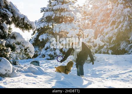 Une jeune femme joue avec son Cocker américain dans la forêt d'hiver parmi les pins enneigés. Banque D'Images