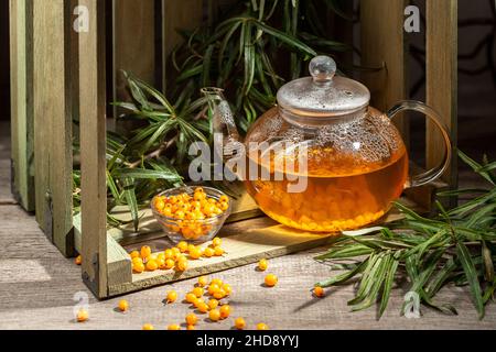 Boisson chaude d'hiver à base de baies de Buckthorn dans une bouilloire en verre sur une table en bois Banque D'Images