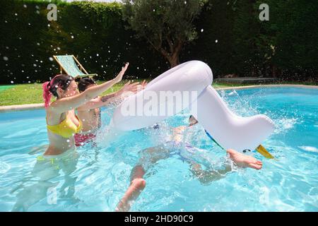 Deux amis qui jettent un homme d'une licorne arc-en-ciel flottent dans la piscine. Banque D'Images