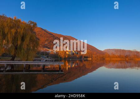 Petit village surplombant le lac pendant un coucher de soleil d'automne avec un saule. Banque D'Images