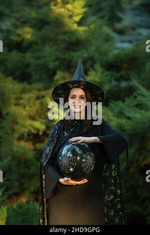 Portrait d'une jeune femme attirante vêtue d'une robe noire avec une cape.Dans les mains d'une balle noire.Une fille aux cheveux foncés et aux yeux verts bruns et au makeu Banque D'Images