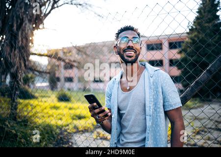 Portrait d'un beau homme latino-américain utilisant son smartphone souriant dans la rue Banque D'Images
