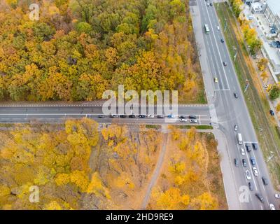 Route panoramique aérienne dans la forêt jaune d'automne.Survolez les voitures en conduisant les rues en crossroad dans le parc de la ville d'automne.Vue sur les arbres à Kharkiv, Ukraine Banque D'Images