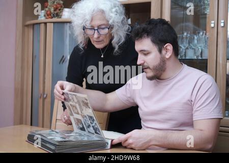 La mère mature et le fils adulte regardent de vieilles photos en noir et blanc dans l'album. Banque D'Images