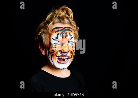 Portrait d'un garçon avec visage de tigre peint avec une expression heureuse, isolé sur fond noir. Banque D'Images