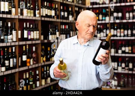 Un retraité sérieux choisit le vin blanc et le vin rouge dans un magasin de spiritueux Banque D'Images