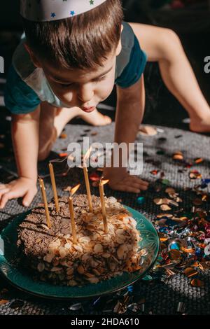 Mignon petit garçon heureux soufflant des bougies allumées sur son gâteau d'anniversaire.Fête Banque D'Images