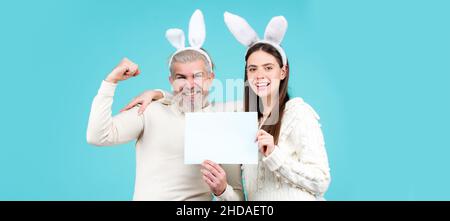 Le couple de Pâques vêtu de costume tenant un tableau blanc vierge pour votre texte.Bannière avec un couple de lapins drôle, espace de copie. Banque D'Images