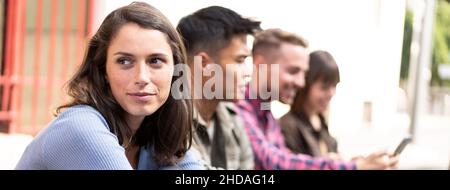 Bannière horizontale ou en-tête avec une jeune femme réfléchie en premier plan et des amis multiculturels heureux sur le fond à l'université de pause Banque D'Images