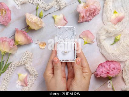 Femme mains tenant une boîte cadeau avec une bague de perle avec des fleurs rose clair et des rubans vintage autour de la vue de dessus Banque D'Images