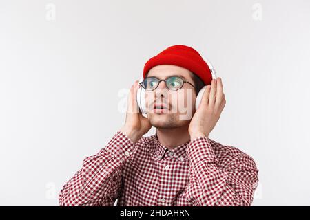 Gros plan portrait de jeune homme branché et débordé à écouter le nouvel album de son groupe préféré, en touchant le casque et en regardant étonnés Banque D'Images