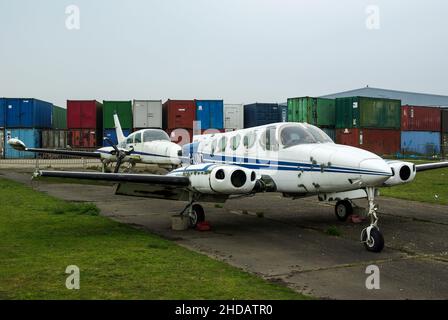 Les avions en décomposition entreposés à l'aérodrome de North Weald, dans l'Essex, au Royaume-Uni, avec des piles de conteneurs d'expédition.Cessna 340 G-LUND et Cessna T310R G-VDIR garés Banque D'Images