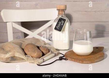 Lait à base de plantes végétaliennes en bouteille et en verre.Lait de pomme de terre de remplacement et tubercules de pomme de terre sur table blanche.Sac de ficelle tricoté avec pommes de terre entières. Banque D'Images