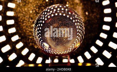 Boule de cristal avec des reflets aux couleurs chaudes en forme de neige et de petits carrés réfléchis sur fond noir, typique pour Noël. Banque D'Images