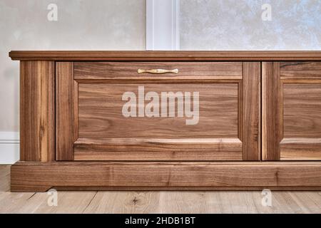 Nouveau meuble TV élégant en placage et bois de noyer massif avec poignées dorées près du mur dans la salle lumineuse vue à angle bas Banque D'Images