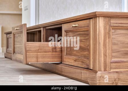 Nouveau meuble TV élégant en placage et bois de noyer massif avec poignées dorées près du mur dans la salle lumineuse vue à angle bas Banque D'Images