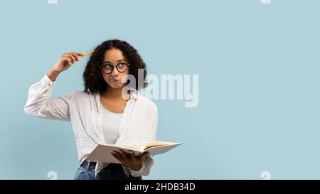 Livre de lecture jeune femme noire réfléchie étudiant, pensant à quelque chose sur fond bleu, bannière avec espace de copie Banque D'Images