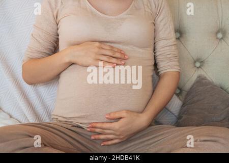 Plan court de femme enceinte tenant le ventre tout en se relaxant sur le canapé à la maison, femme enceinte assise sur le canapé à l'intérieur et touchant doucement le ventre.Prég Banque D'Images