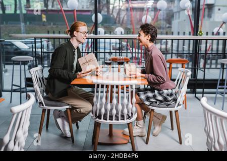 Jeune couple tenant des cadeaux près de verres de vin dans le café de l'hôtel Banque D'Images