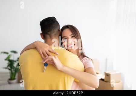 Concept d'hypothèque et de réinstallation.Bonne dame du Caucase embrassant son petit ami, tenant la clé de la nouvelle maison Banque D'Images