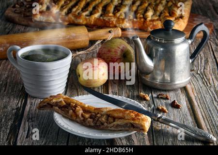 Une tranche de tarte aux pommes avec des noix de strudel et une tasse de tisane chaude Banque D'Images