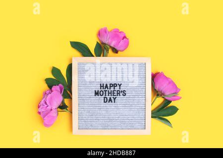 Bonne journée des mères.Tableau de lettres avec cadre en fleurs de pivoine sur fond jaune. Banque D'Images
