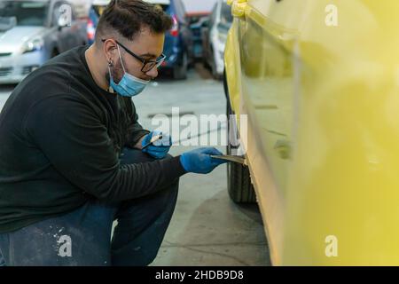 Mécanicien automobile répare une voiture jaune avec du mastic pour peinture dans un atelier Banque D'Images