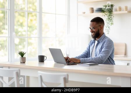 Joyeux homme afro-américain du millénaire avec une barbe en lunettes bavardant à distance, travaillez sur ordinateur seul Banque D'Images