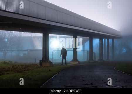 Une figure à capuche effrayante avec un visage caché, debout sous un pont.Sur une nuit effrayante, brumeuse, hivers Banque D'Images