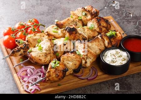 Délicieux kebabs de poulet sur brochettes de légumes frais et deux sauces gros plan sur un plateau en bois sur fond de béton gris. Horizontal Banque D'Images