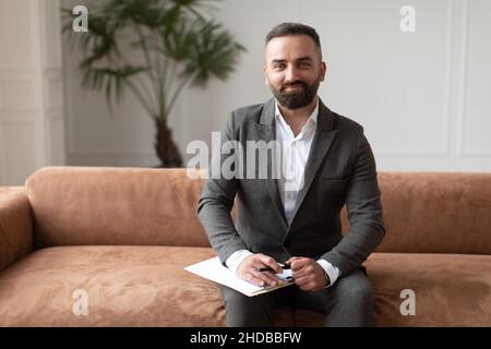 Portrait d'un thérapeute homme confiant en costume assis sur un canapé Banque D'Images