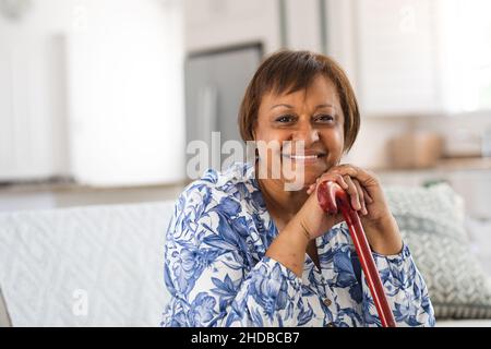 Portrait d'une femme âgée afro-américaine heureuse avec canne à pied dans le salon à la maison Banque D'Images