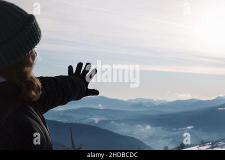 La main de la femme se dirige vers un paysage magnifique.Belle vue sur les Alpes en hiver.Ensoleillé, givré, enneigé.Mise au point sélective Banque D'Images