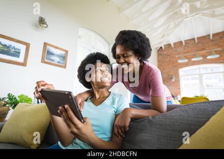 Bonne mère regardant l'adolescente en utilisant une tablette numérique sur le canapé à la maison Banque D'Images