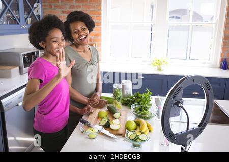 Bonne adolescente fille et mère vlogging tout en préparant le jus sain dans la cuisine à la maison Banque D'Images