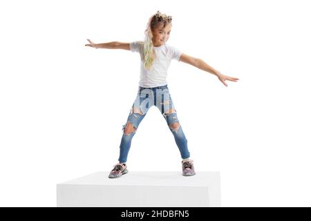 Portrait complet d'une fille souriante dans des vêtements décontractés debout sur une grande boîte isolée sur fond blanc de studio. Concept d'enfance heureuse. Banque D'Images