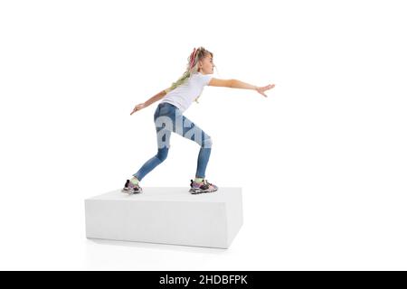 Portrait complet d'une fille souriante dans des vêtements décontractés debout sur une grande boîte isolée sur fond blanc de studio. Concept d'enfance heureuse. Banque D'Images