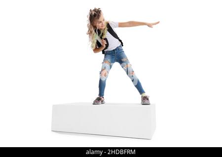 Portrait complet d'une fille souriante dans des vêtements décontractés debout sur une grande boîte isolée sur fond blanc de studio. Concept d'enfance heureuse. Banque D'Images