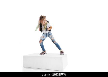 Portrait complet d'une fille souriante dans des vêtements décontractés debout sur une grande boîte isolée sur fond blanc de studio. Concept d'enfance heureuse. Banque D'Images