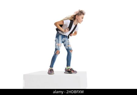 Portrait complet d'une fille souriante dans des vêtements décontractés debout sur une grande boîte isolée sur fond blanc de studio. Concept d'enfance heureuse. Banque D'Images