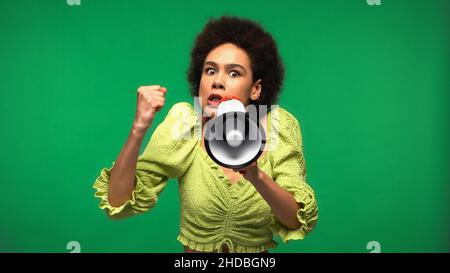 une femme afro-américaine en colère proteste tout en tenant le haut-parleur et en regardant la caméra isolée sur le vert Banque D'Images