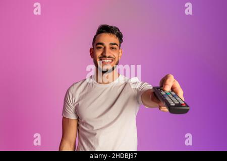 Jeune garçon arabe positif regardant la télévision, changer de chaîne avec télécommande dans la lumière de néon Banque D'Images