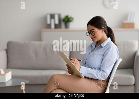 Psychologue professionnel écrivant dans le presse-papiers, assis sur une chaise au bureau, offrant des services de conseils professionnels Banque D'Images