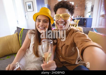 Portrait d'un jeune couple biracial heureux prenant le selfie tout en appréciant la fête à la maison Banque D'Images