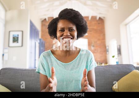 Portrait d'une femme afro-américaine joyeuse qui fait des gestes tout en expliquant sur appel vidéo à la maison Banque D'Images